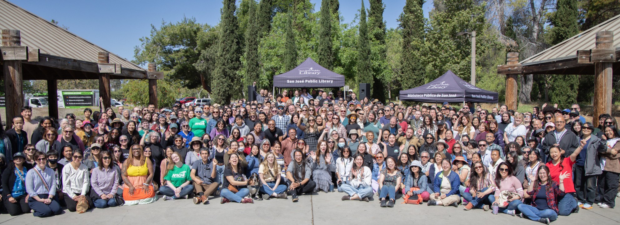 A large group of San José Public Library staff posing together at Lake Cunningham Park, with some standing, kneeling, and sitting on a sunny day for their Spring All-Staff Inservice.