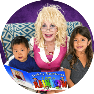 Dolly parton in pink shirt sits with two children reading a book.