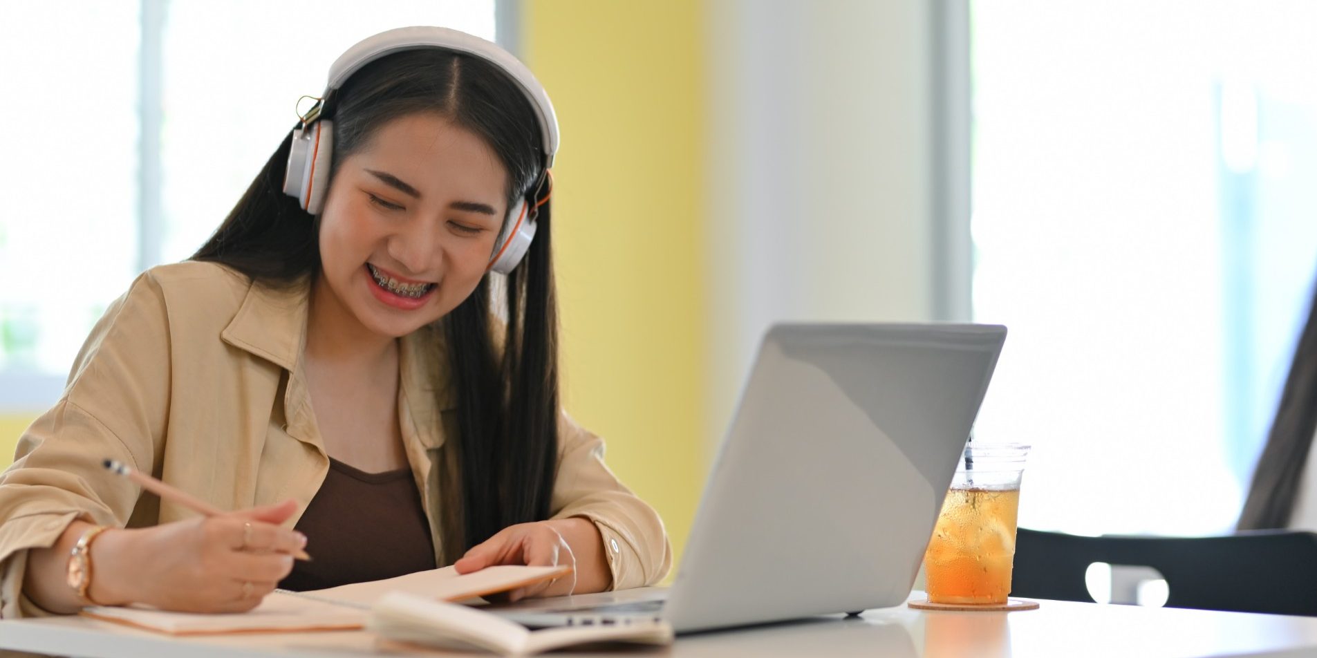 Student with headphone smiling while doing home working with stationery and laptop